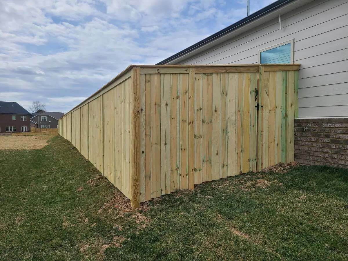 Full privacy wood fence and gate with cap and trim design installed around the side of a home